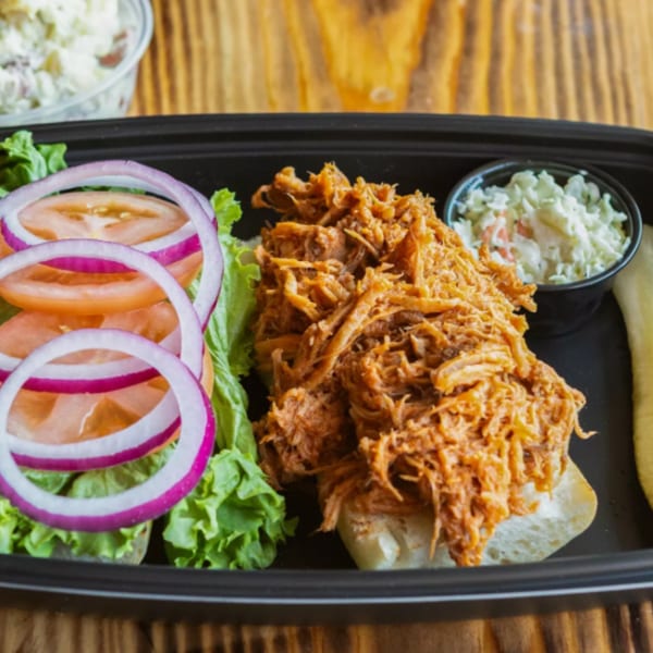 Ludy's BBQ pulled pork sandwich with lettuce, tomato, onion, coleslaw, and a pickle.