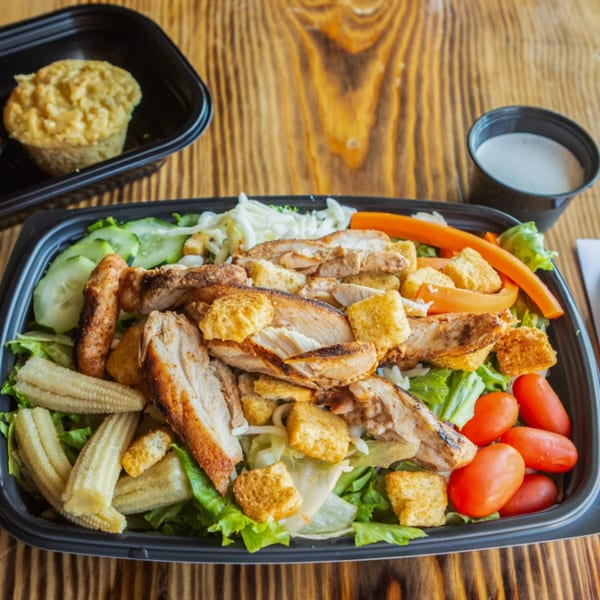 Ludy's BBQ chicken salad with baby corn, tomatoes, cucumbers, and croutons, with a side of cornbread and dressing.