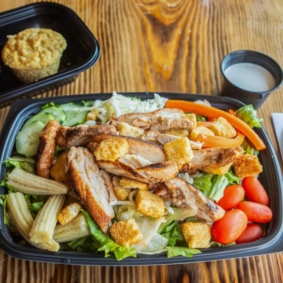 Ludy's BBQ chicken salad with baby corn, tomatoes, cucumbers, and croutons, with a side of cornbread and dressing.