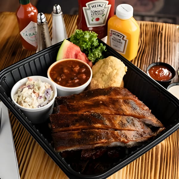Ludy's BBQ ribs meal with coleslaw, baked beans, cornbread, watermelon, and lettuce.