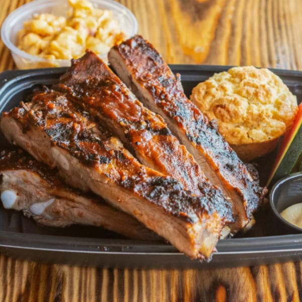 Ludy's BBQ ribs with a side of mac and cheese and a corn muffin on a wooden table.