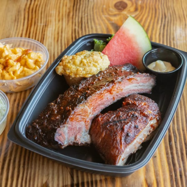 Ludy's BBQ ribs with a side of cornbread, watermelon, mac and cheese, and coleslaw.