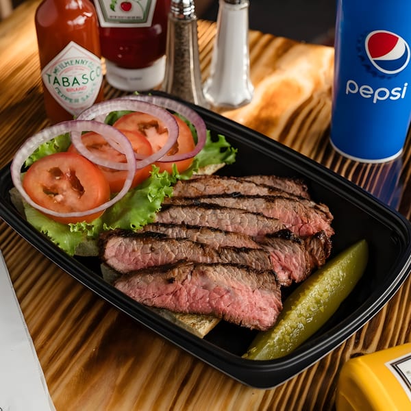 Ludy's BBQ sliced steak sandwich with lettuce, tomato, onion, and a pickle spear.