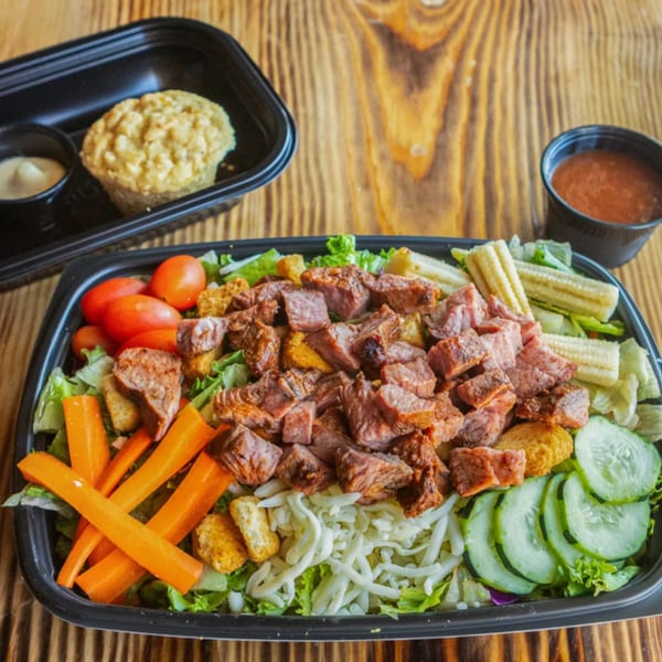 Ludy's BBQ steak salad with baby corn, carrots, tomatoes, cucumbers, cheese, and a cornbread muffin.