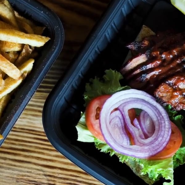 Ludy's BBQ ribs with sauce, lettuce, tomato, and onion, next to a container of fries.
